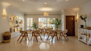 A spacious dining area with a round table and six chairs, surrounded by shelves with decorative items and a large window with natural light. - Noya By Dhara Hotels (Giza)