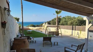 Un porche cubierto con muebles de madera, un barril grande y vista al mar.