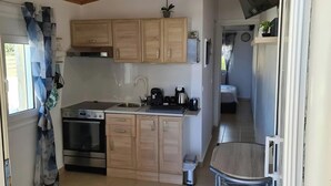 Una cocina con armarios de madera, una estufa y un lavamanos. Hay un cubo de basura pequeño y una silla en la esquina.