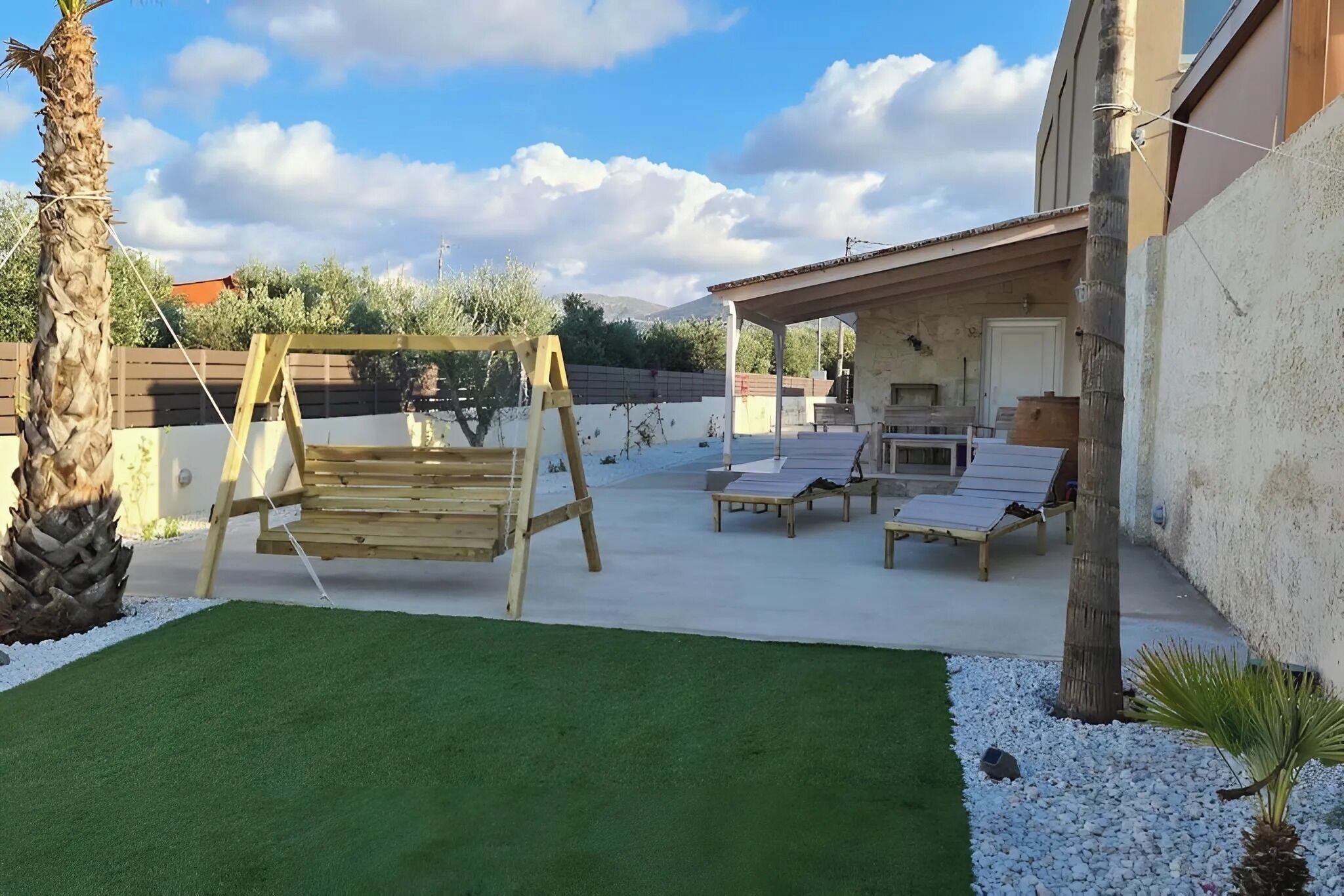 A patio area with a swing set, lounge chairs, and a covered seating area.