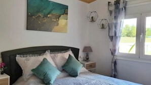 Un dormitorio con cama, mesita de noche, lámpara, ventana con cortinas y un cuadro en la pared.