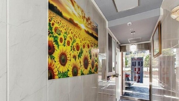A hallway with a sunflower mural on the wall, a glass door leading outside, and a marble floor. - Thema Motel (Seoul)