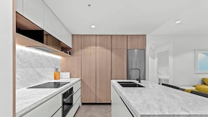 A modern kitchen with marble countertops, wooden cabinets, and a stainless steel refrigerator.