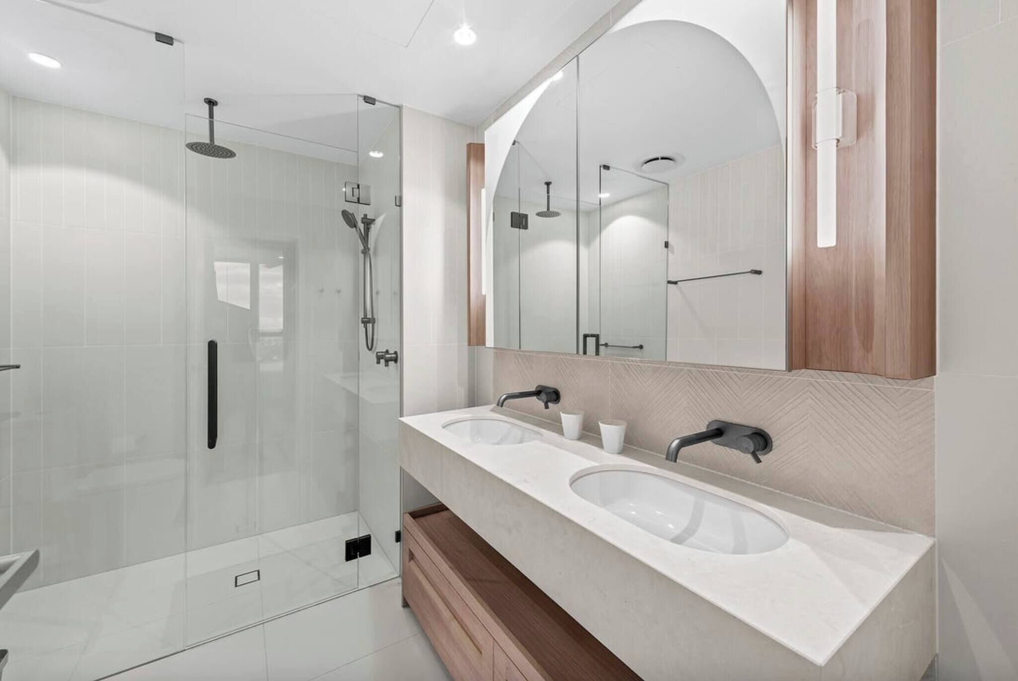 Een moderne badkamer met een douchecabine van glas, twee wastafels en een grote spiegel.