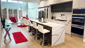 A modern kitchen with a marble island, stainless steel appliances, and a red accent rug. - Trinity Two Luxury Home (Dallas)
