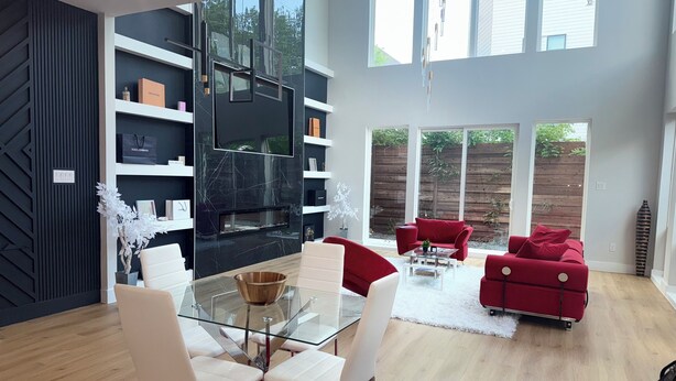 A modern living room with a glass dining table, white chairs, red sofas, and a black fireplace. - Trinity Two Luxury Home (Dallas)