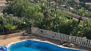 Una piscina de borde curvo, rodeada por un patio empedrado con sillas de descanso y una mesa.