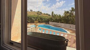 Vista desde una ventana a una piscina, con vistas a un paisaje montañoso y árboles.