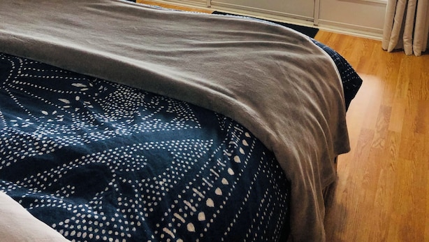 Une chambre à coucher avec un lit, une chaise et une vue sur une étendue d’eau, visible à travers de grandes portes.