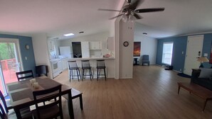 Un salón amplio con mesa de comedor, sillas, ventilador de techo y cocina al fondo.