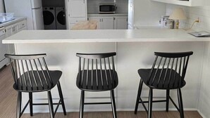 Una cocina moderna con armarios blancos, una isla central con taburetes de bar, un microondas y una lavadora.
