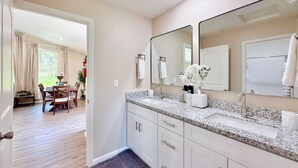 Un baño moderno con encimera de granito, espejos dobles en tocador y lavabo blanco.