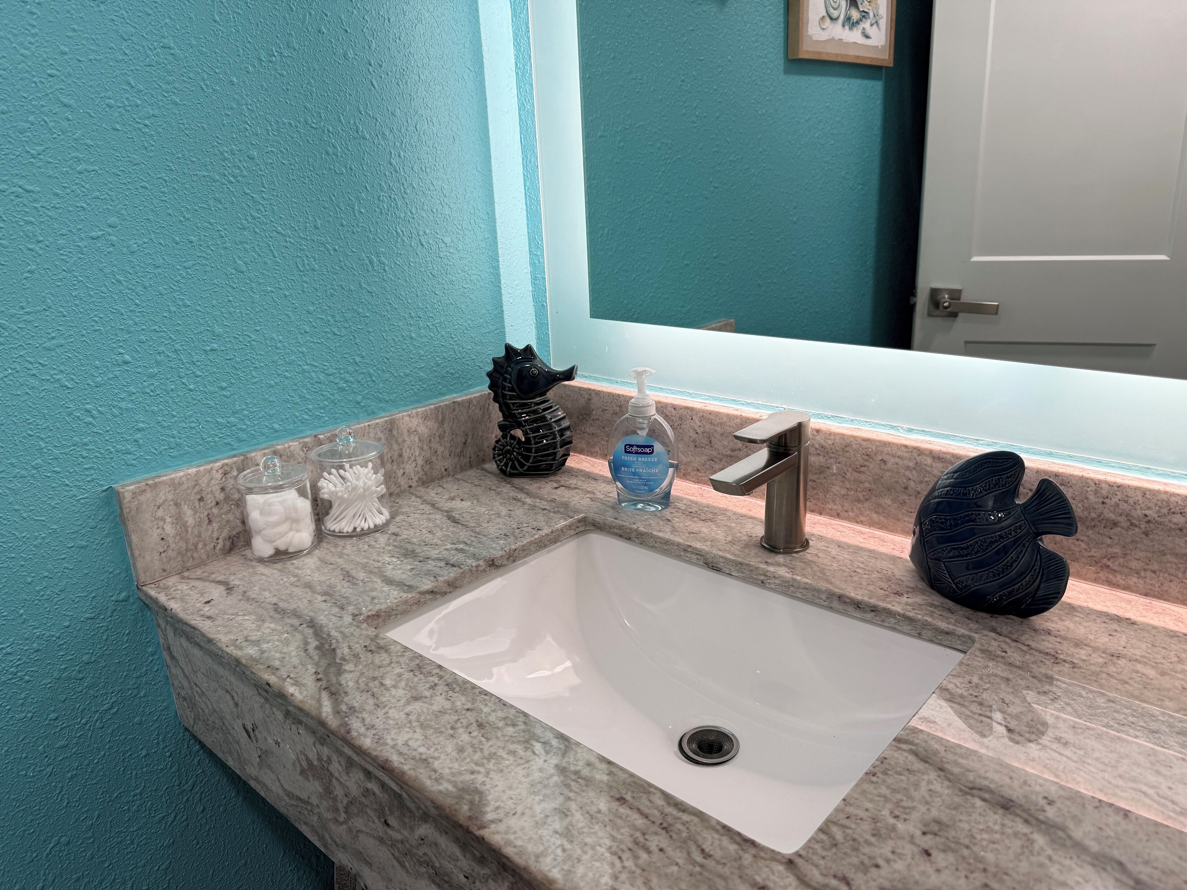 A bathroom sink with a marble countertop, a seahorse decoration, a soap dispenser, and a fish-shaped soap dish.