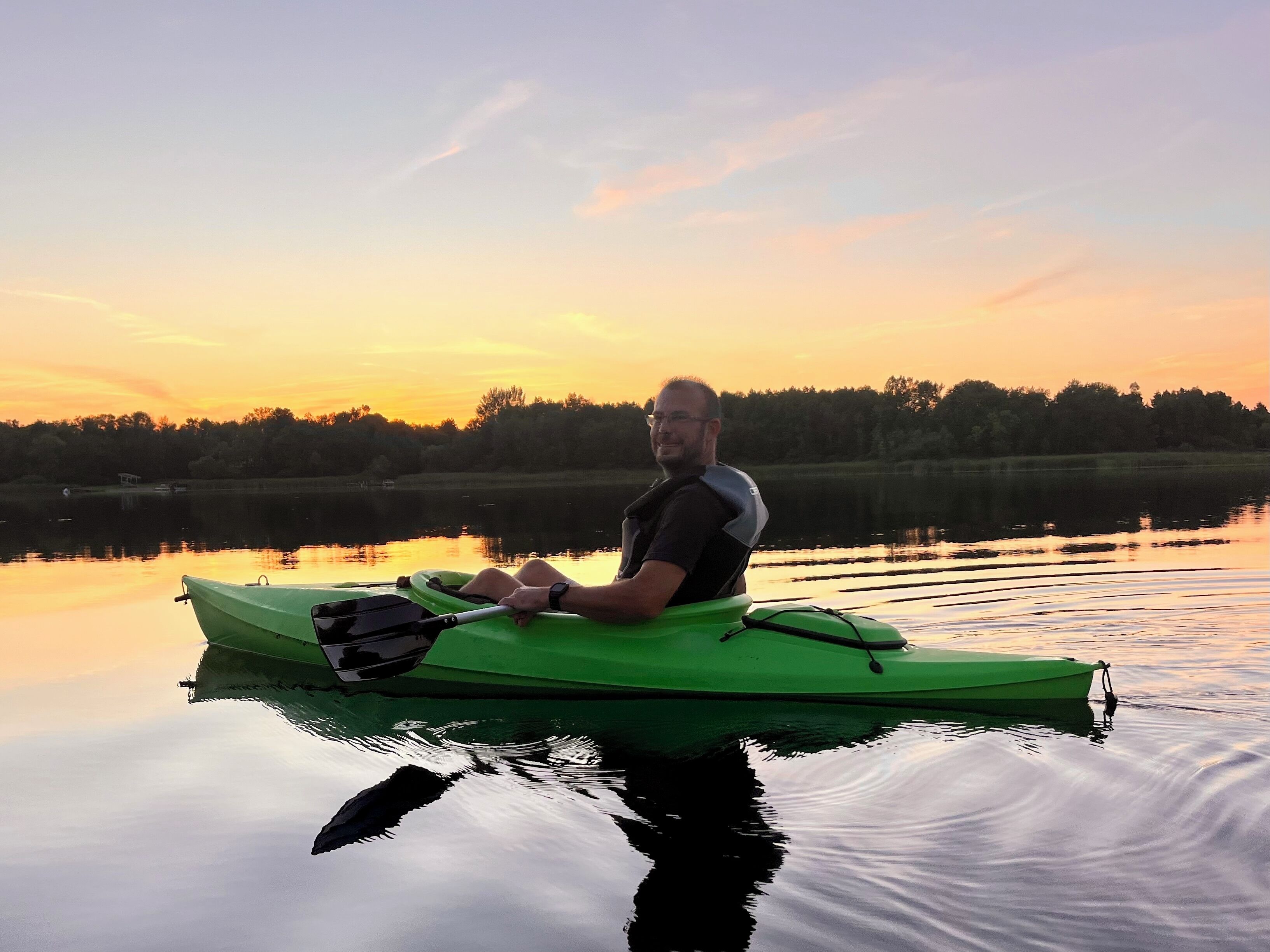 Een persoon in een groene kano op een kalm meer tijdens de zonsondergang.