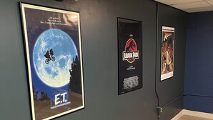 A room with dark walls, a wooden floor, and three movie posters: ET, Jurassic Park, and Raiders of the Lost Ark.