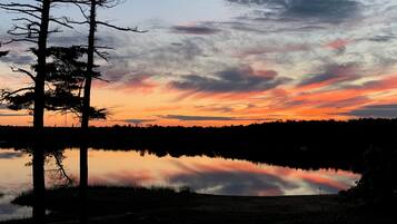 A sunset over a calm lake with trees silhouetted against the sky.