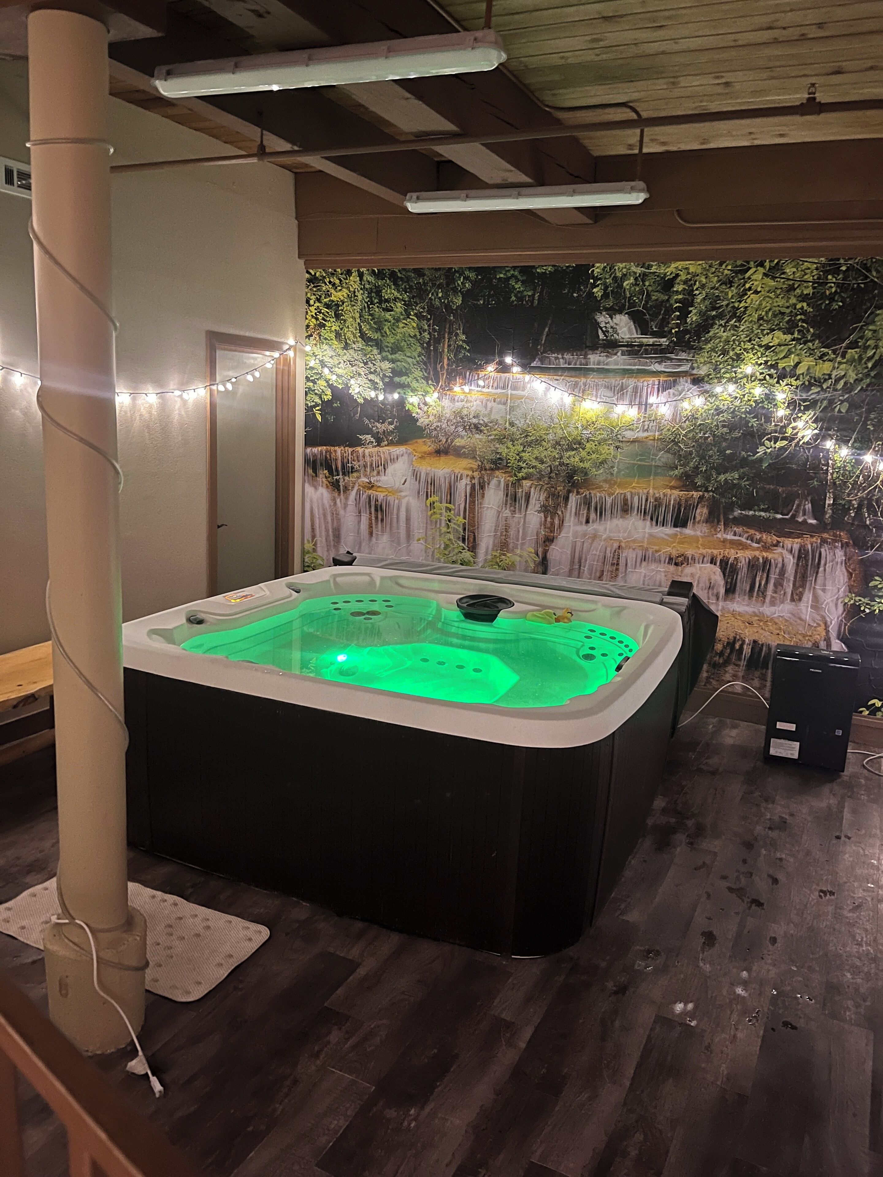 Un bain à remous avec une cascade en arrière-plan, un plancher en bois et des guirlandes lumineuses.