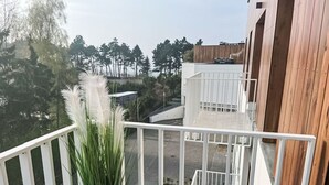 Een balkon met een bloempot en uitzicht op een gebouw met een houten gevel en een witte balustrade.