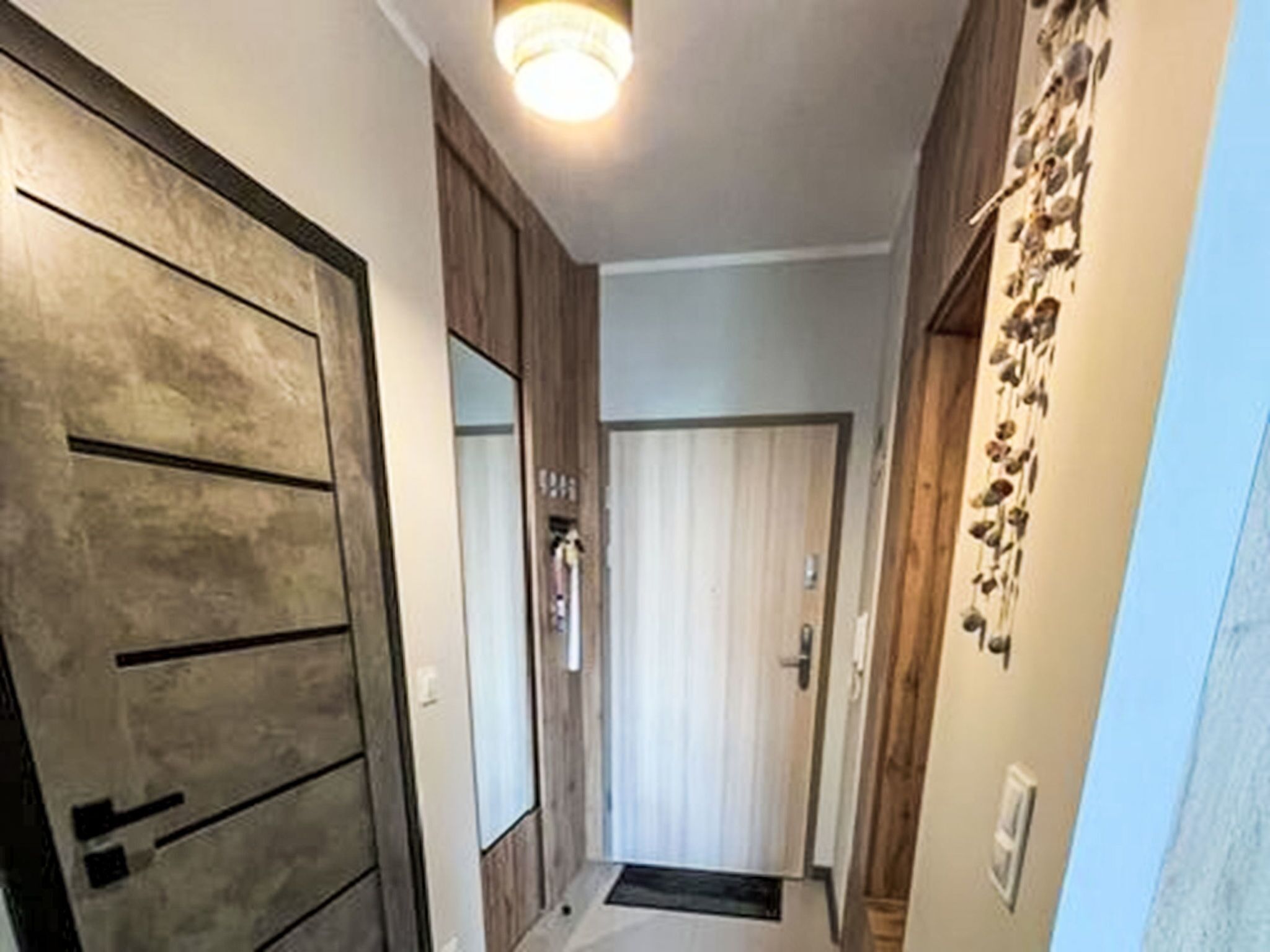 Un couloir avec des portes en bois, un miroir et un élément décoratif fixé au mur.