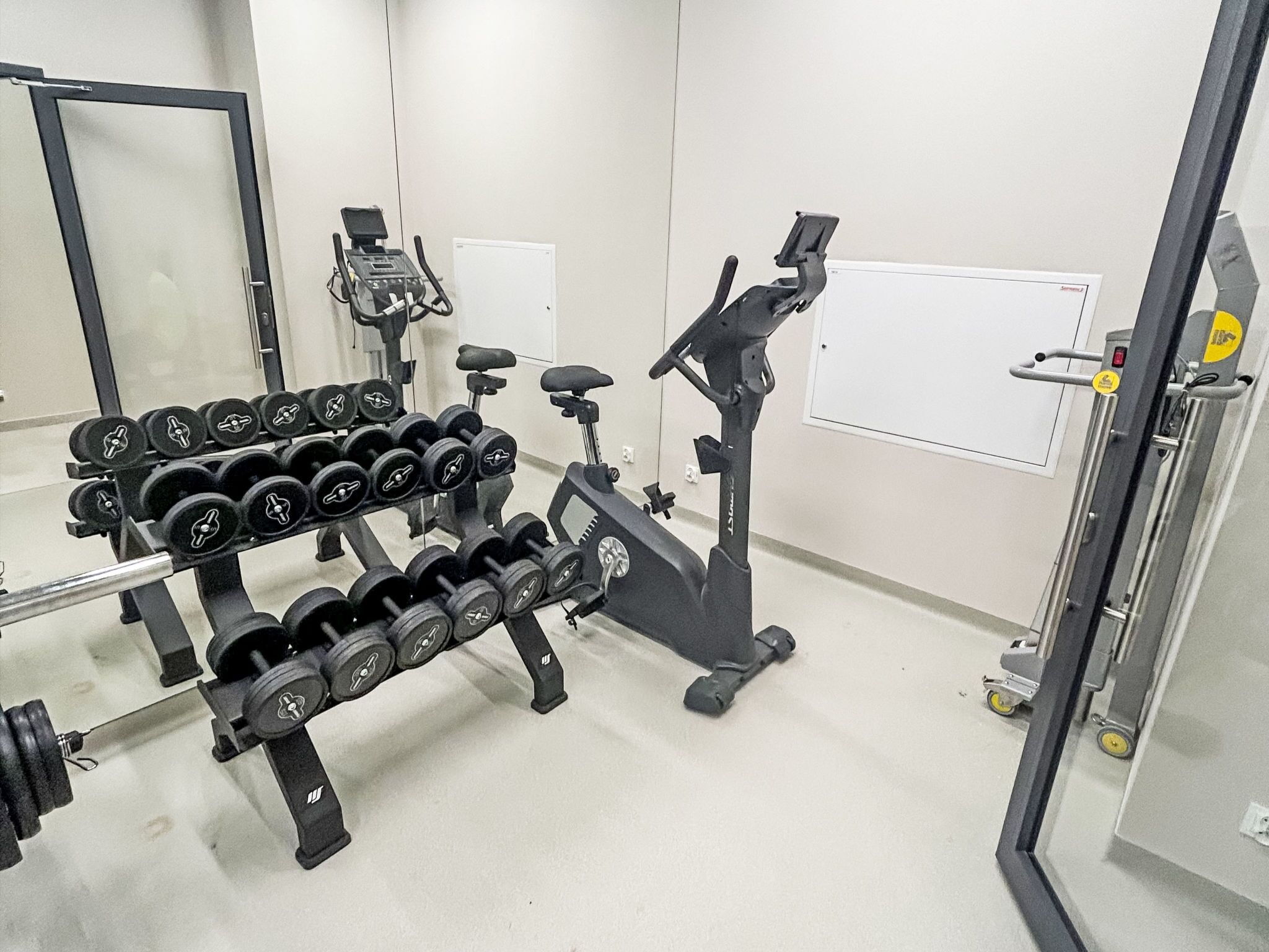 Uma academia com halteres, uma bicicleta ergométrica e uma esteira.