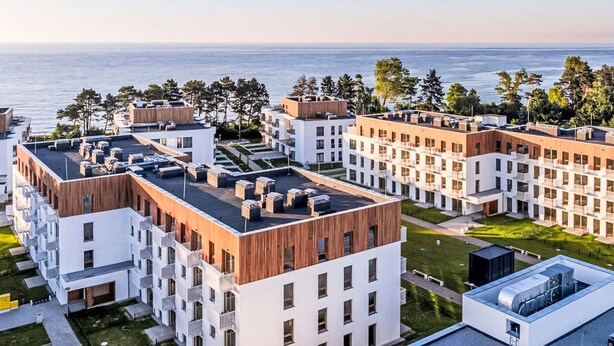 Een modern appartementencomplex met meerdere gebouwen, dakterrassen en uitzicht op zee.