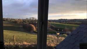 Vista a través de una ventana de un paisaje rural con campos, una cerca y un farol.