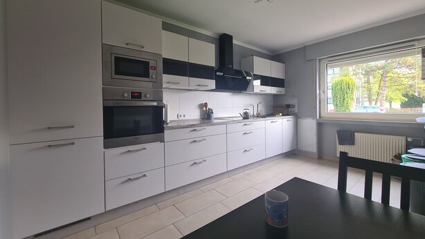 A modern kitchen with white cabinets, stainless steel appliances, and a black countertop. - Comfortable Home (Ennigerloh)