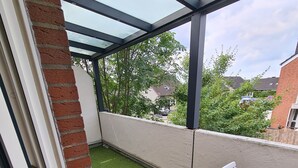 Un balcón con césped artificial, una silla blanca y vistas a casas vecinas.