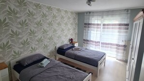 A bedroom with two single beds, a ceiling fan, a nightstand with a lamp, and a window with curtains. - Comfortable Home (Ennigerloh)