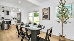 A modern kitchen with white cabinets, a stainless steel refrigerator, and a dining area with a round table set for four. - Media Room & Patio - Downtown View- 4 Bedrooms (Houston)