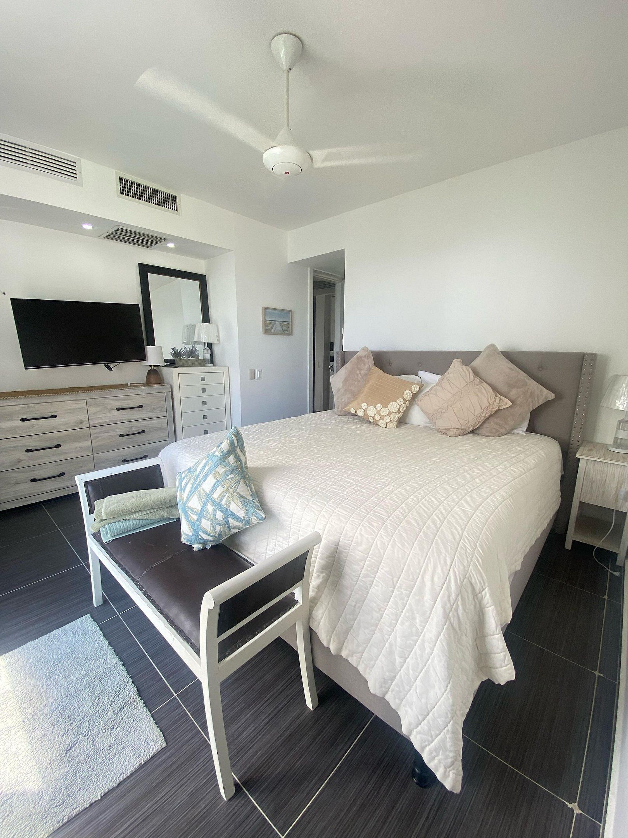 A modern bedroom with a bed, bedside tables, a TV, and a ceiling fan.