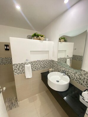 Un baño moderno con un espejo grande, un lavamanos redondo y un salpicadero de azulejos.