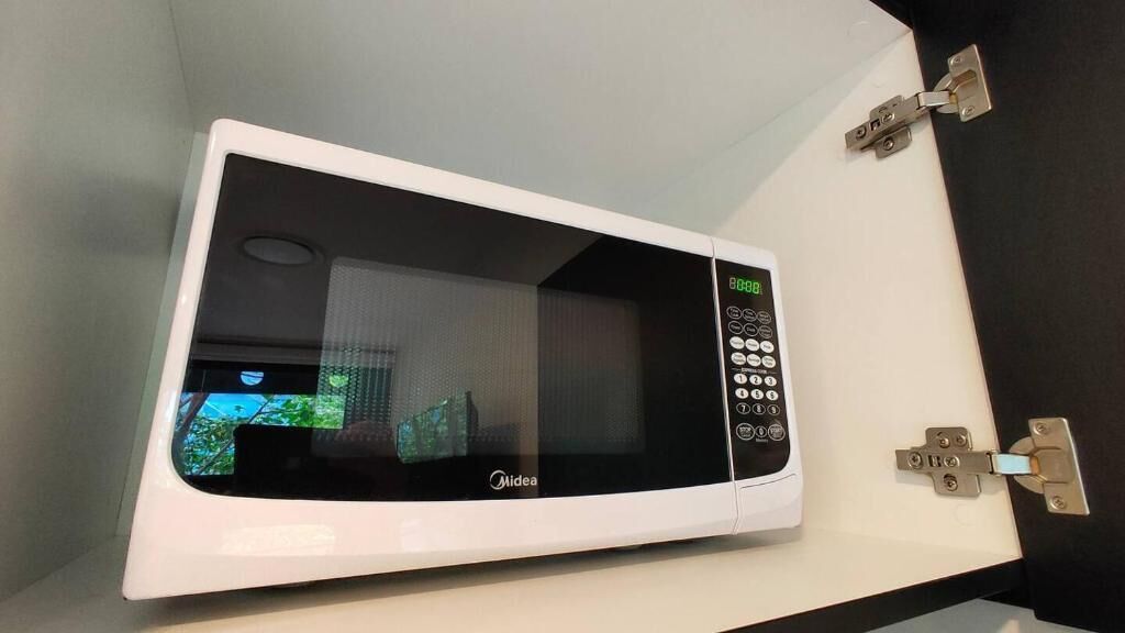 Forno a microonde bianco con display digitale e pannello comandi, montato su una parete bianca con porta nera.