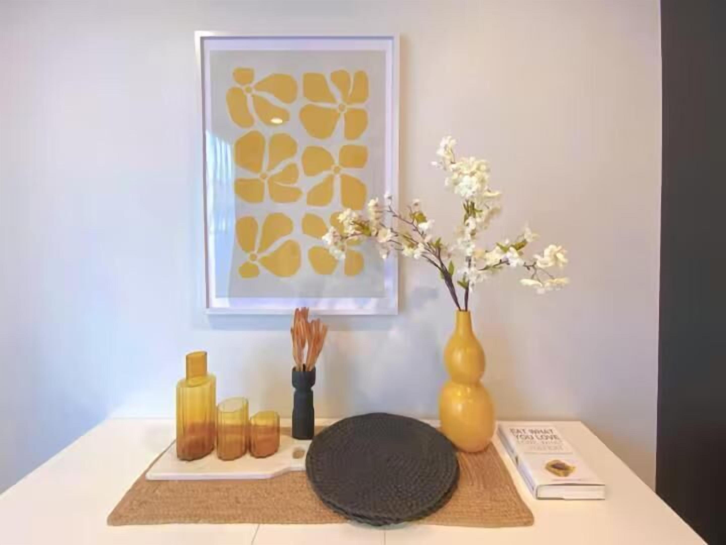 A table with a framed artwork, a vase with flowers, a book, and candle holders.