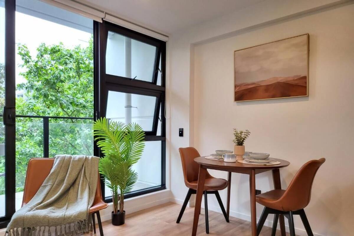 Comedor con una mesa redonda, dos sillas, una planta en maceta y una ventana con vistas a zonas verdes.