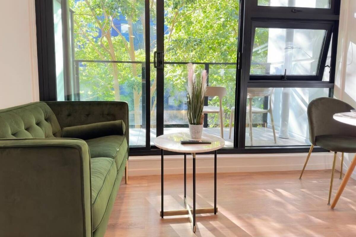 Una habitación con un sofá verde, una pequeña mesa redonda con una planta y una silla.