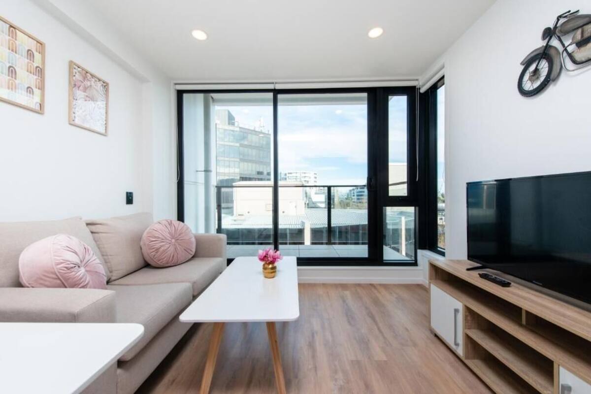 Una sala de estar moderna con un sofá, una mesa de centro, un televisor y un ventanal con vistas a la ciudad.