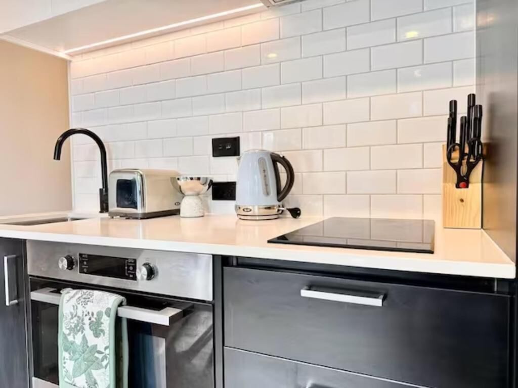 A modern kitchen with white tiled backsplash, stainless steel appliances, and a knife block.