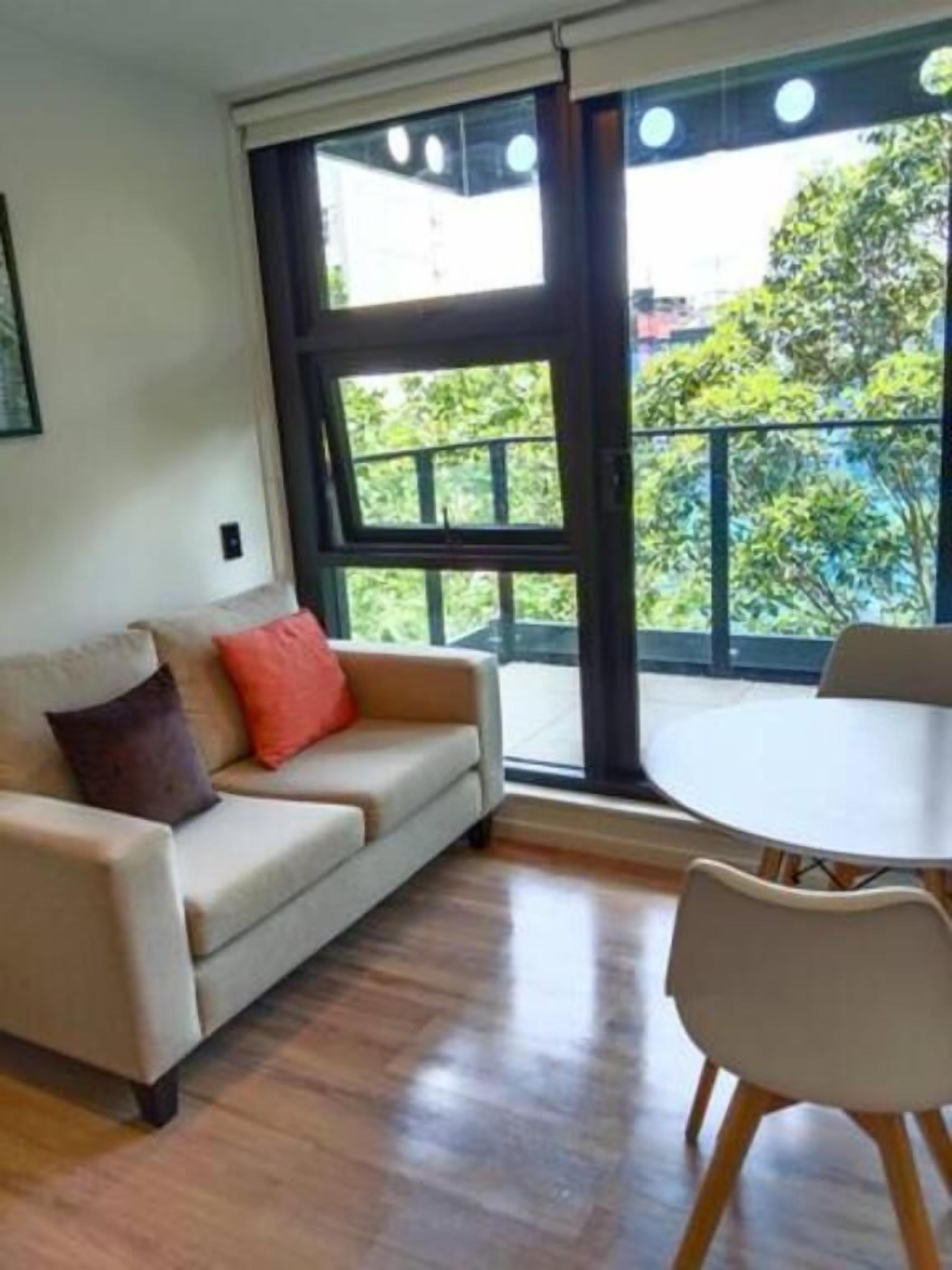 A living room with a sofa, a round table, and a view of greenery outside.