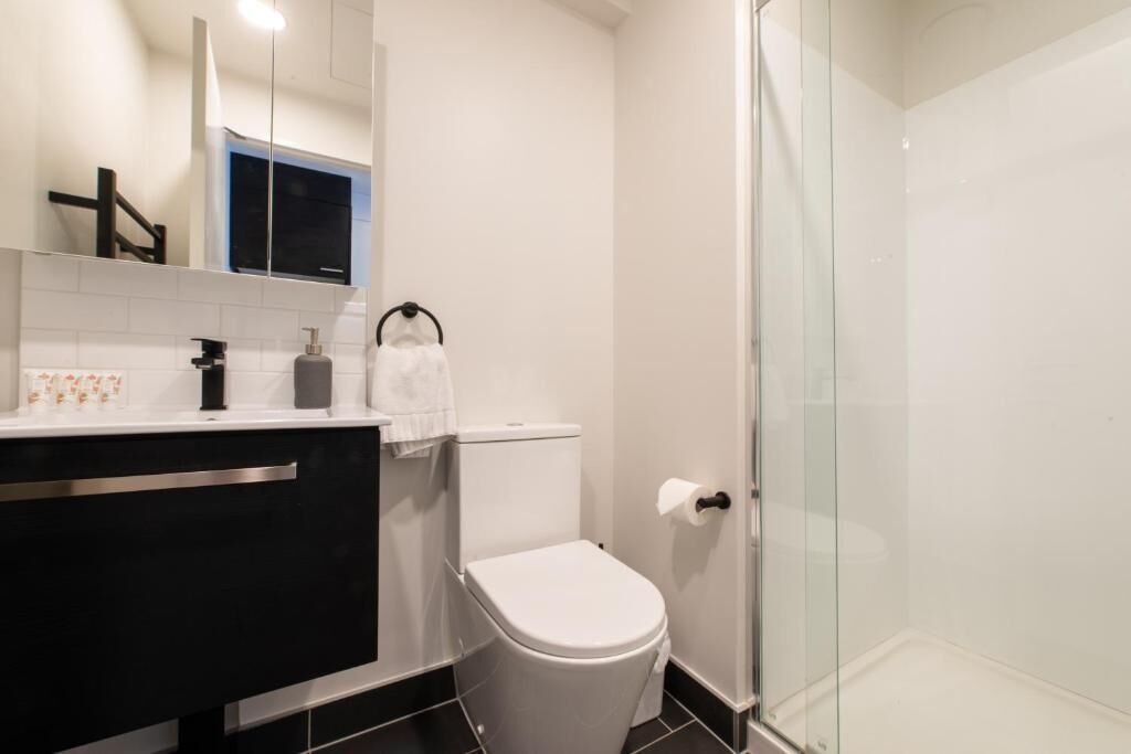 Un baño moderno con cabina de ducha de vidrio, inodoro blanco y tocador negro con espejo.