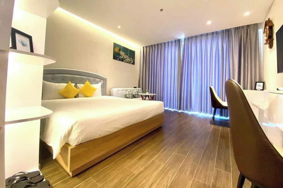 Ein modernes Hotelzimmer mit einem großen Bett, einem Schreibtisch, einem Stuhl und Blick auf die Stadt durch das Fenster.