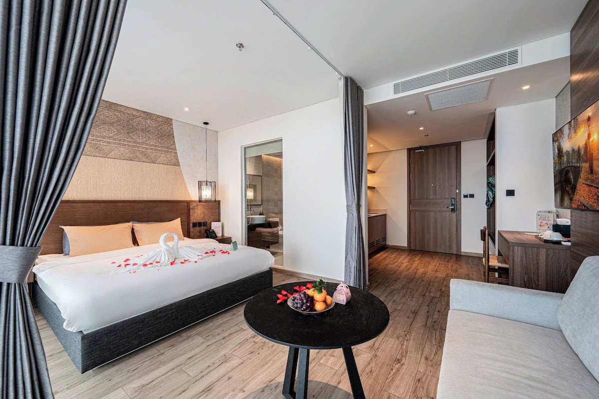 Ein modernes Hotelzimmer mit einem großen Bett, einem runden Tisch mit Obst und Blick auf die Stadt.