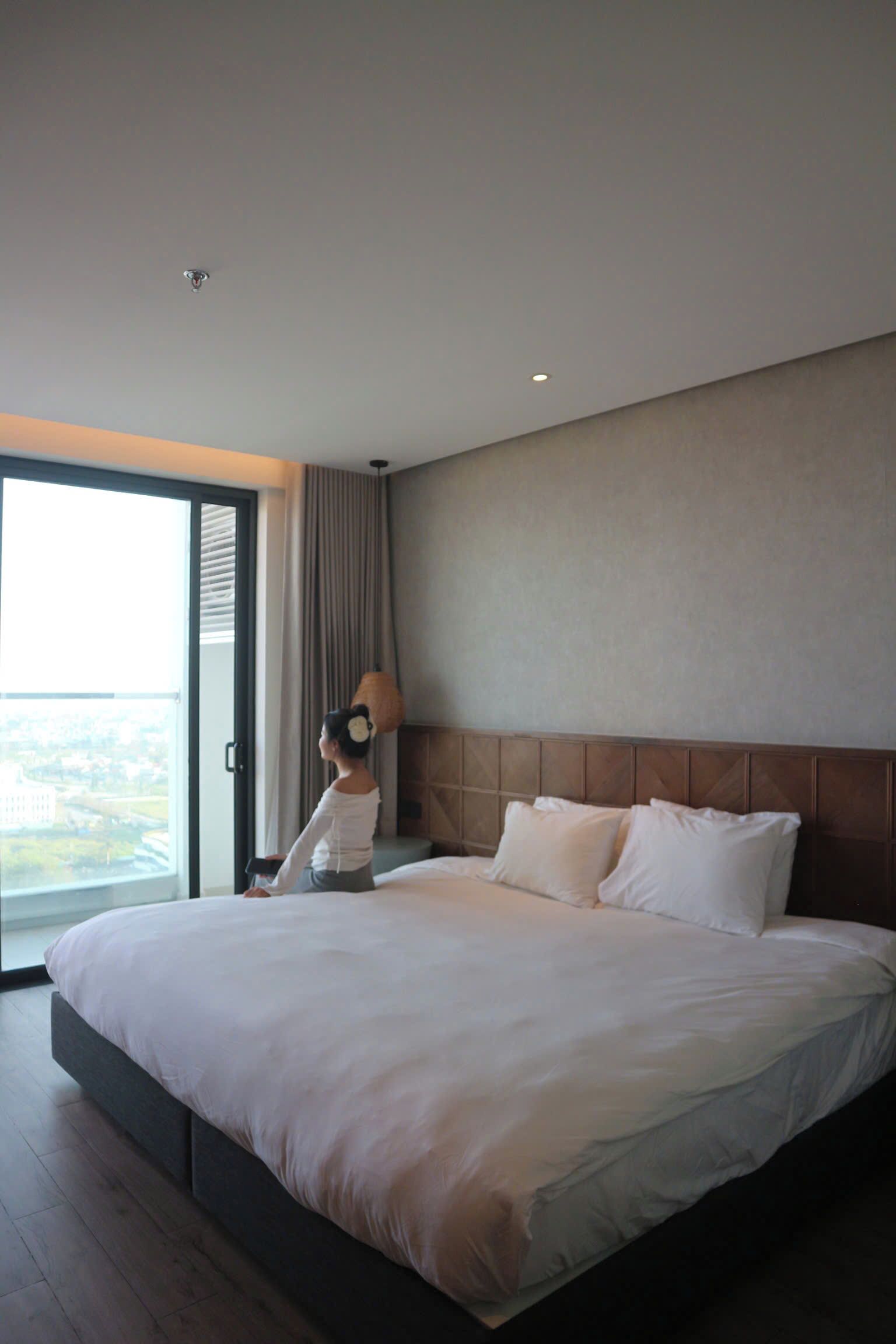 Habitación de hotel con una cama grande, vistas a través de la puerta de vidrio y una lámpara en el techo.