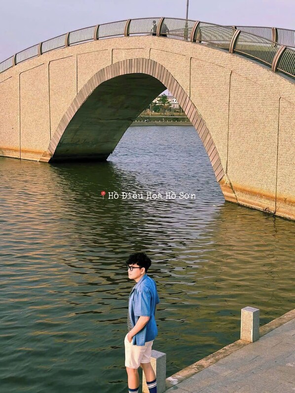 A stone bridge over a calm river with a person standing on the riverbank. - DaVanie- Apec Mandala Phu Yen (Tuy Hoa)