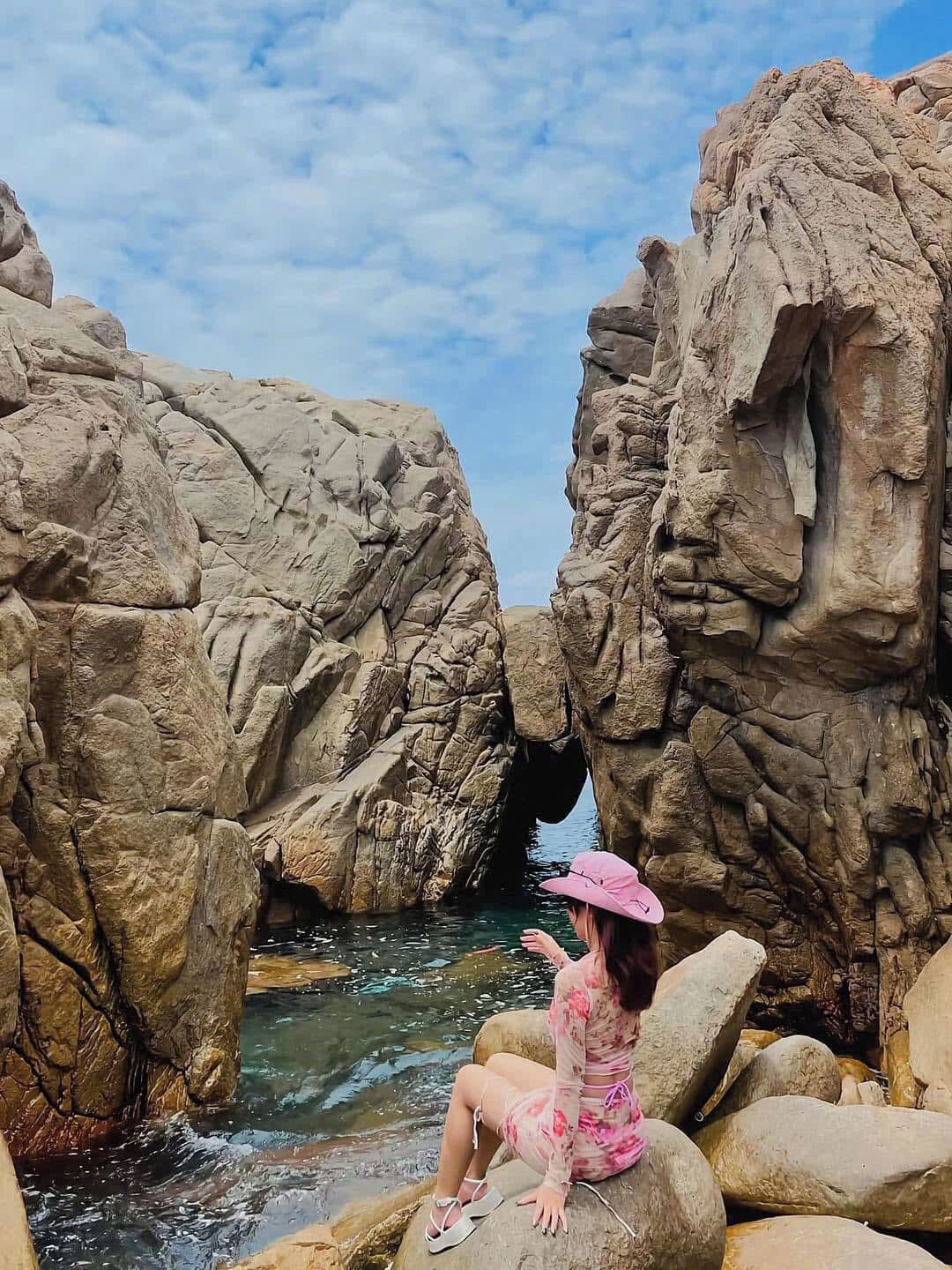 A person sitting on a rock by a rocky coastline with a clear sky.