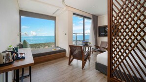 Une chambre d’hôtel avec une grande fenêtre donnant sur la mer, un lit, un bureau avec un ordinateur portable et une chaise.