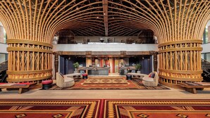 Un hall d’entrée spacieux avec un haut plafond en bambou, un comptoir d’accueil central et un tapis à motifs.