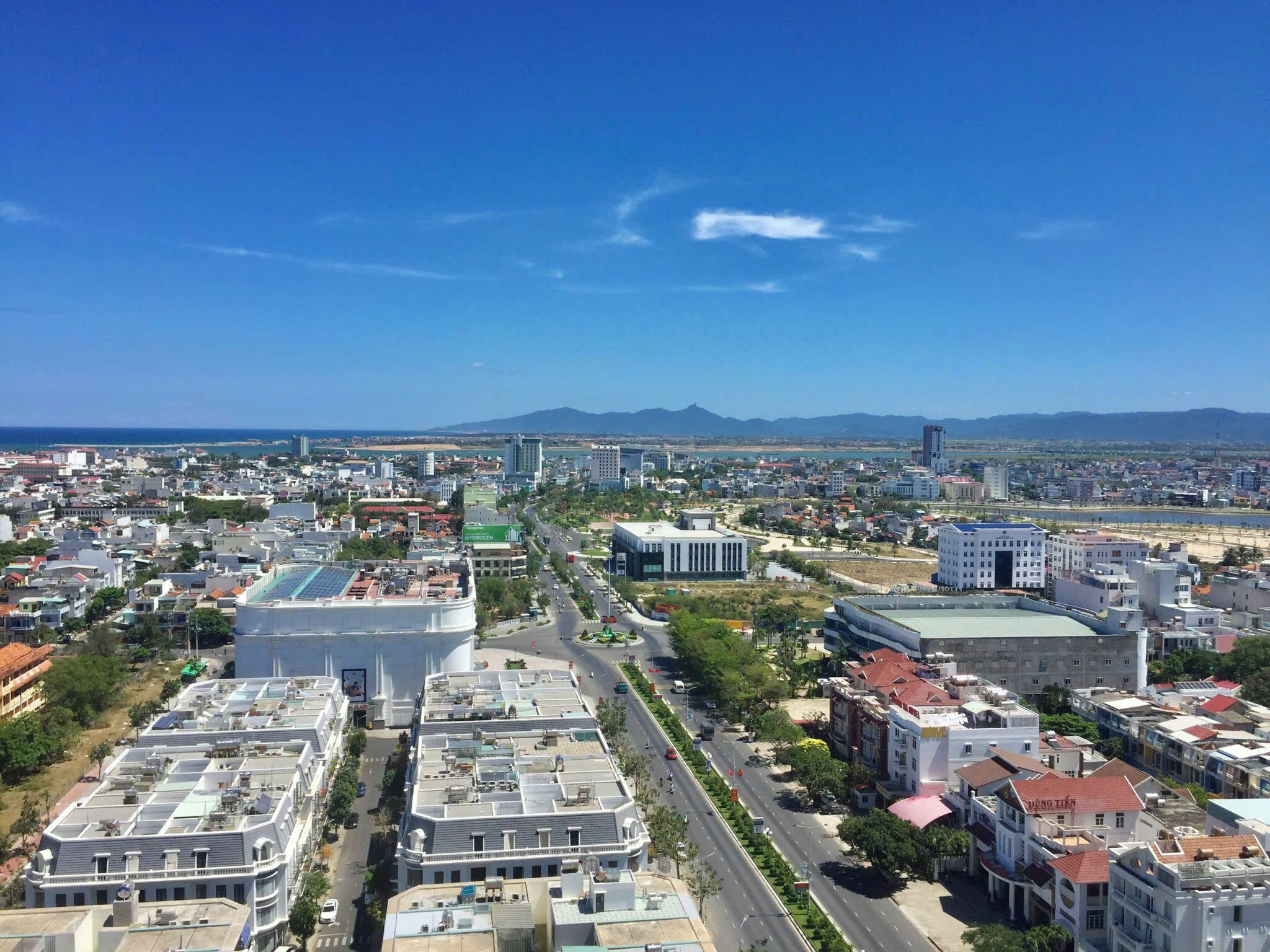 A cityscape with modern buildings, a wide road, and a distant mountain range.