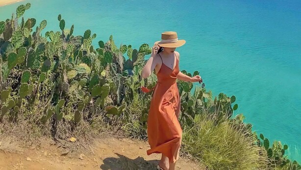 Une personne se trouve dans un paysage désertique, avec une vue sur une plage et l’océan.