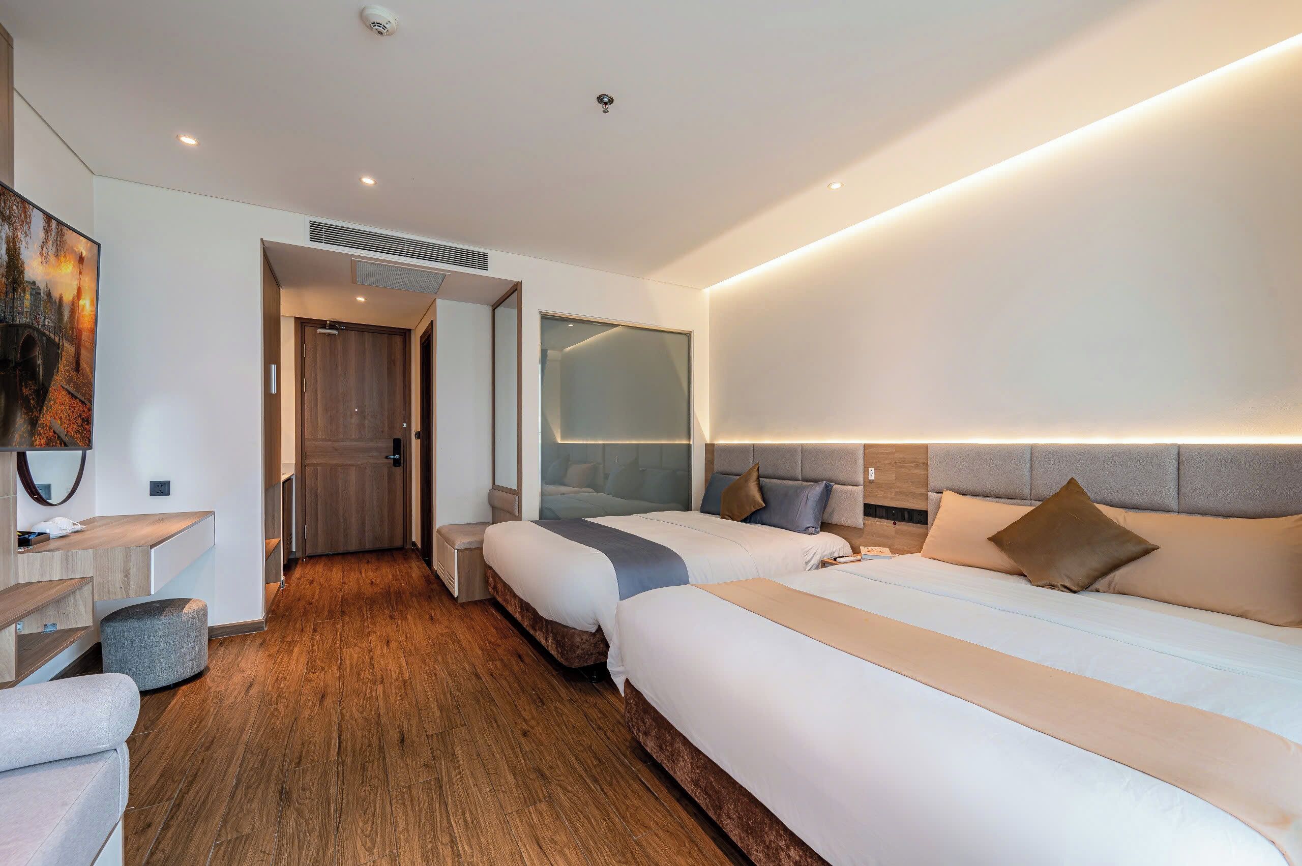 A modern hotel room with two beds, a desk, and a large mirror.